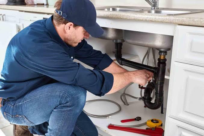 A plumber working under a kitchen sink, adjusting pipes and fixtures.