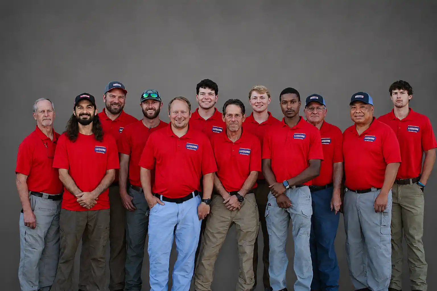 A group of technicians wearing red shirts, standing together in front of a gray background.