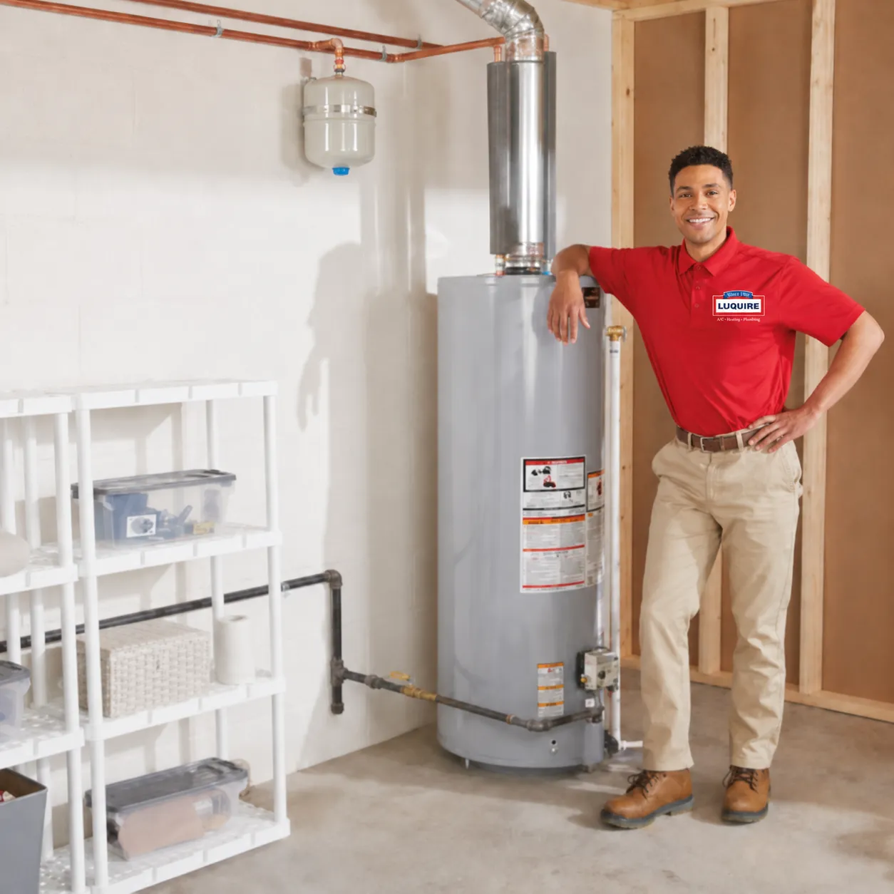 A person in a red shirt stands next to a large, gray traditional water heater. Beside it, there is a modern, compact tankless water heater installed on a wall.